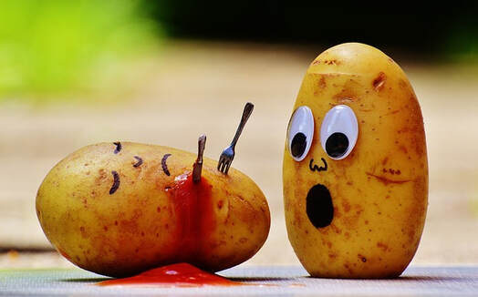 A posed picture of two raw potatoes, both given faces. One potato has been stabbed with a miniature fork and lies in a pool of ketchup. The other potato is upright and has a shocked expression.